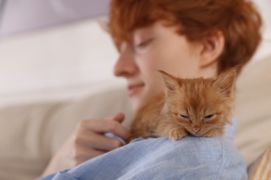 Redhead teenage boy with cute ginger kitten indoors, selective focus