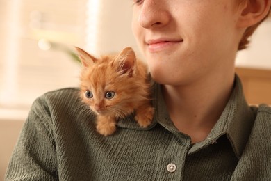 Photo of Teenage boy with his cute ginger kitten indoors, closeup