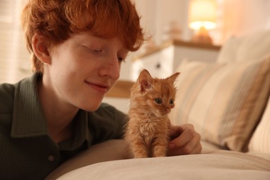 Photo of Redhead teenage boy with cute ginger kitten on sofa indoors