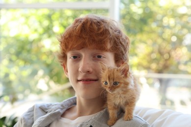 Photo of Redhead teenage boy with cute ginger kitten indoors