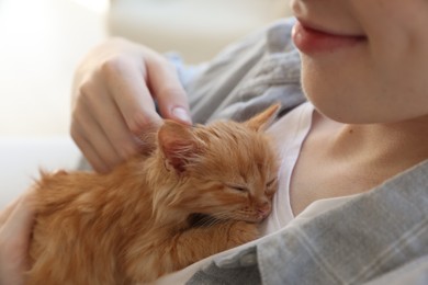 Photo of Teenage boy with his cute ginger kitten indoors, closeup