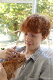 Redhead teenage boy with cute ginger kitten indoors