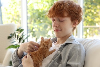 Photo of Redhead teenage boy with cute ginger kitten indoors