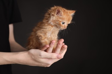 Photo of Teenage boy holding cute ginger kitten on black background, closeup