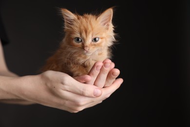 Teenage boy holding cute ginger kitten on black background, closeup