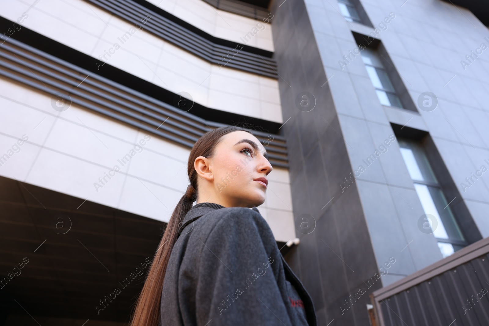 Photo of Beautiful young woman with black coat posing outdoors, low angle view