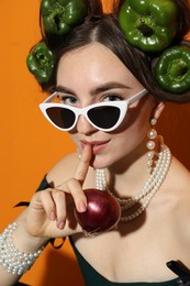 Young woman with peppers in her hair, sunglasses and onion on orange background, closeup