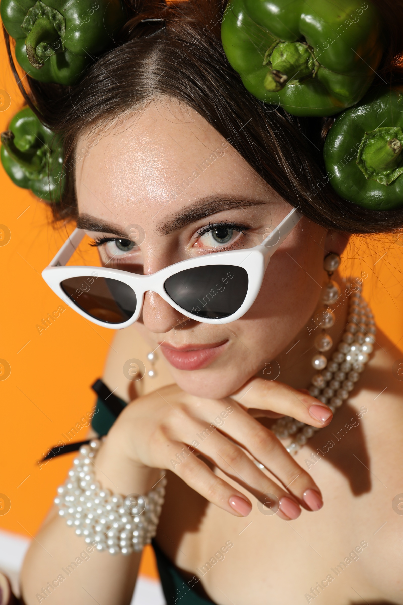 Photo of Young woman with peppers in her hair and sunglasses on orange background, closeup