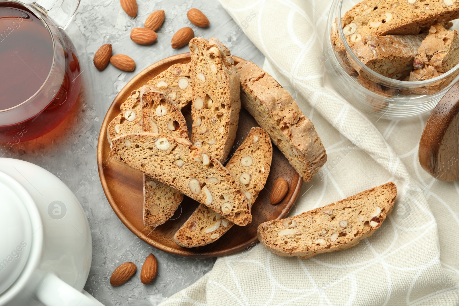 Photo of Traditional Italian almond biscuits (Cantucci), nuts and tea on grey textured table, flat lay