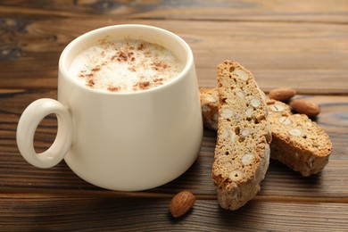 Photo of Traditional Italian almond biscuits (Cantucci), nuts and cup of coffee on wooden table, closeup