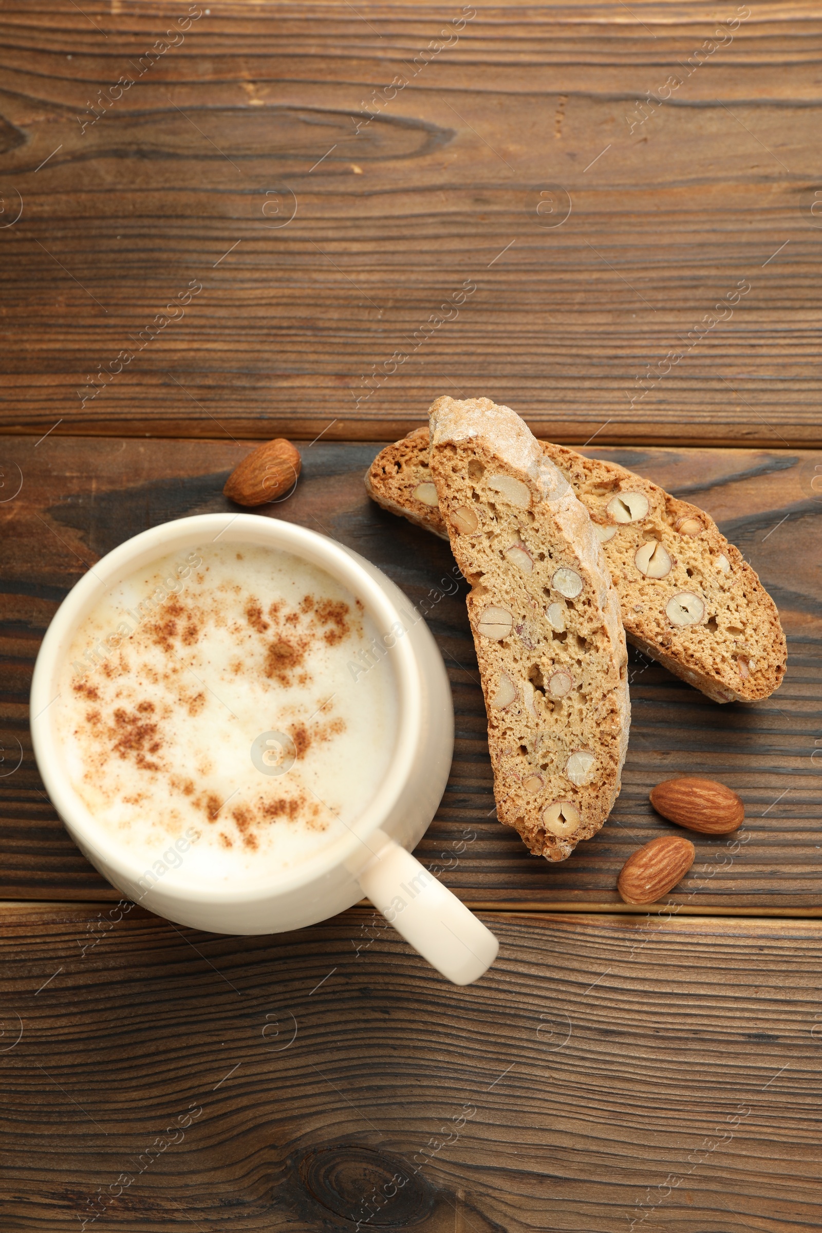 Photo of Traditional Italian almond biscuits (Cantucci), nuts and cup of coffee on wooden table, flat lay