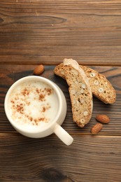 Photo of Traditional Italian almond biscuits (Cantucci), nuts and cup of coffee on wooden table, flat lay