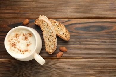 Photo of Traditional Italian almond biscuits (Cantucci), nuts and cup of coffee on wooden table, flat lay. Space for text