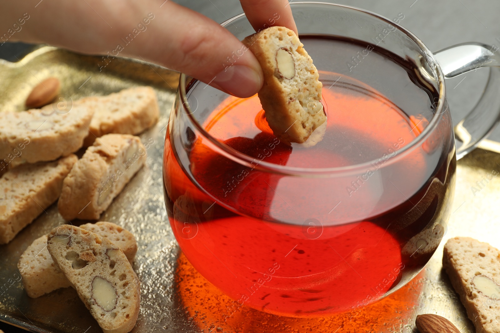 Photo of Woman dipping traditional Italian almond biscuit (Cantucci) into cup of tea at table, closeup