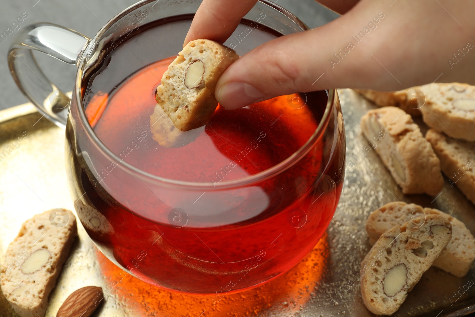 Photo of Woman dipping traditional Italian almond biscuit (Cantucci) into cup of tea at table, closeup