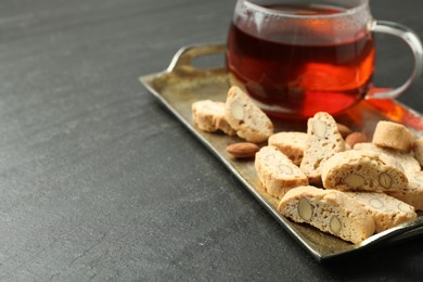 Photo of Traditional Italian almond biscuits (Cantucci), nuts and cup of tea on grey textured table, closeup. Space for text