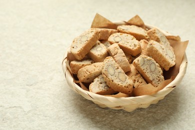 Photo of Traditional Italian almond biscuits (Cantucci) in wicker bowl on light textured table, closeup