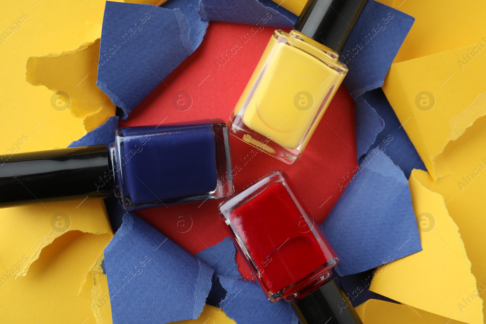 Photo of Bottles of nail polish on red background, top view through hole in color paper