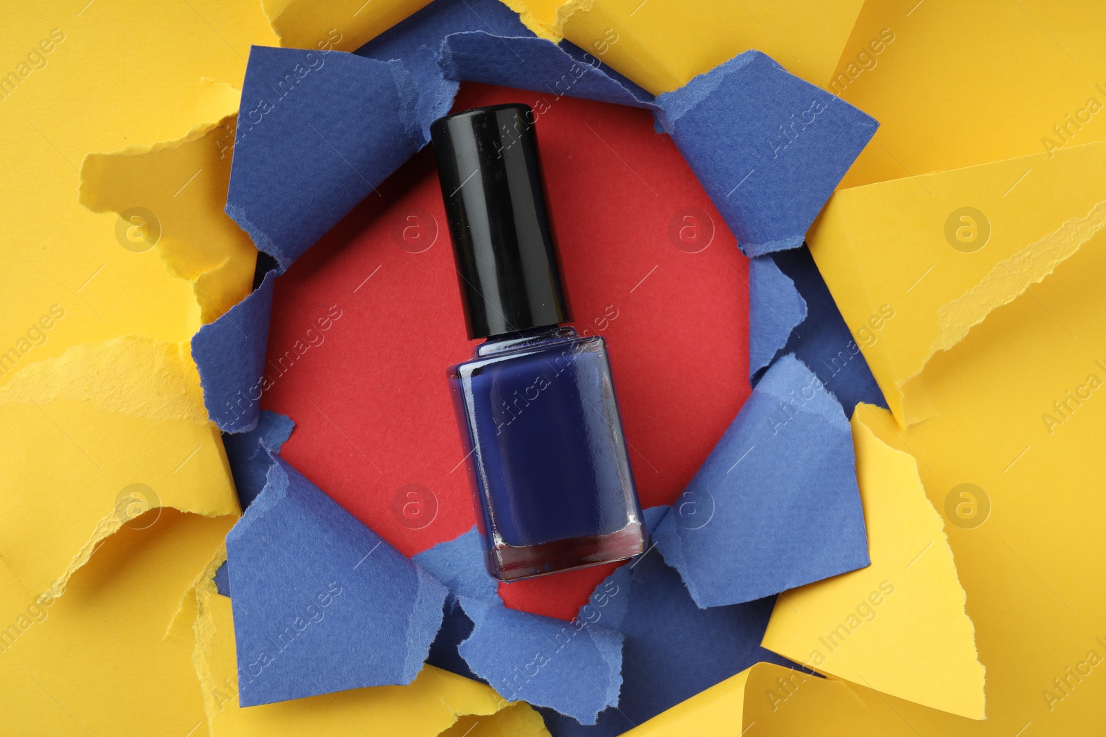 Photo of Bottle of nail polish on red background, top view through hole in color paper