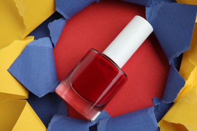 Photo of Bottle of nail polish on red background, above view through hole in color paper