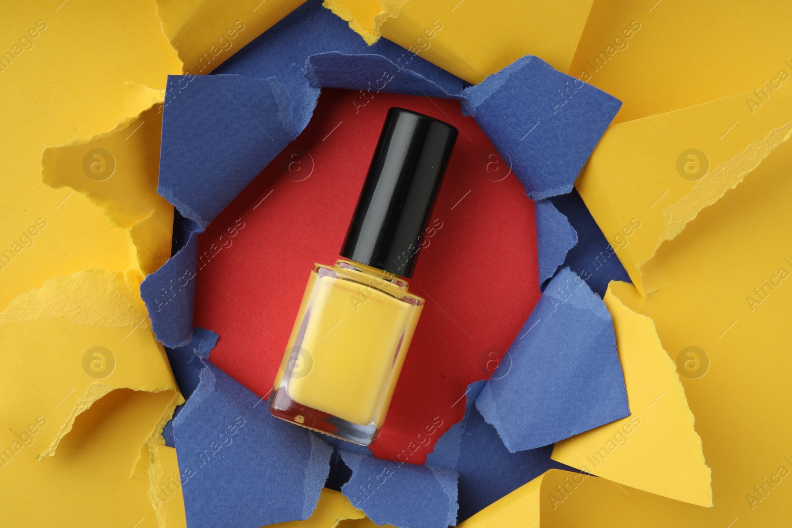 Photo of Bottle of nail polish on red background, top view through hole in color paper