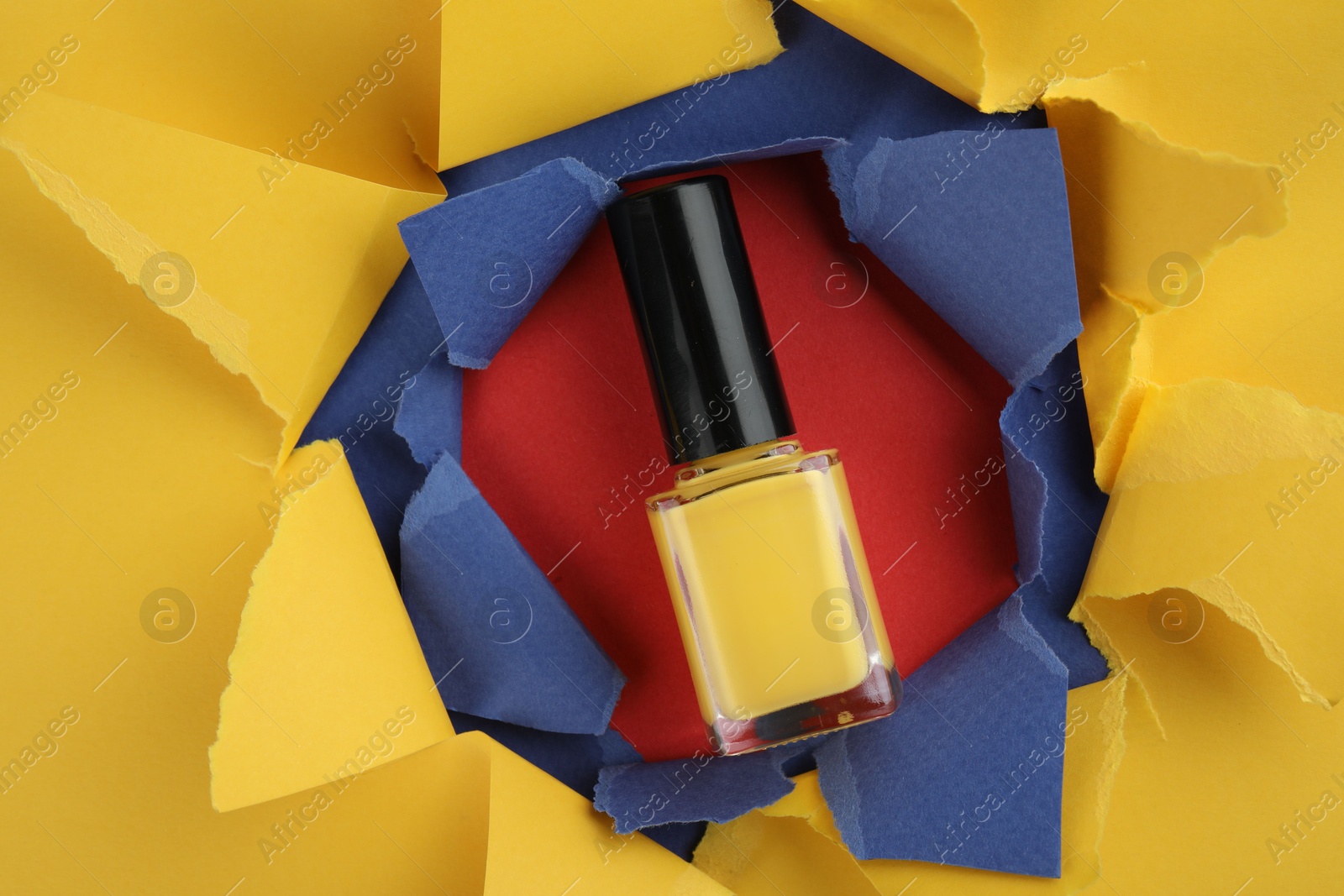 Photo of Bottle of nail polish on red background, top view through hole in color paper