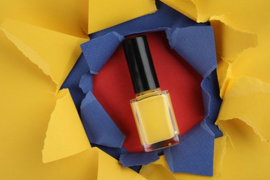 Photo of Bottle of nail polish on red background, top view through hole in color paper