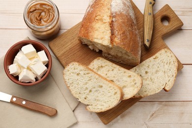 Photo of Cut bread, butter, peanut butter and knives on wooden table, flat lay