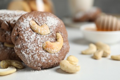 Photo of Tasty chocolate cookies with cashew and powdered sugar on white table, closeup