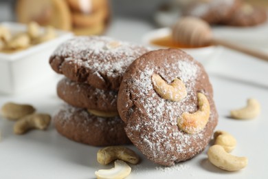 Photo of Tasty chocolate cookies with cashew and powdered sugar on white table, closeup