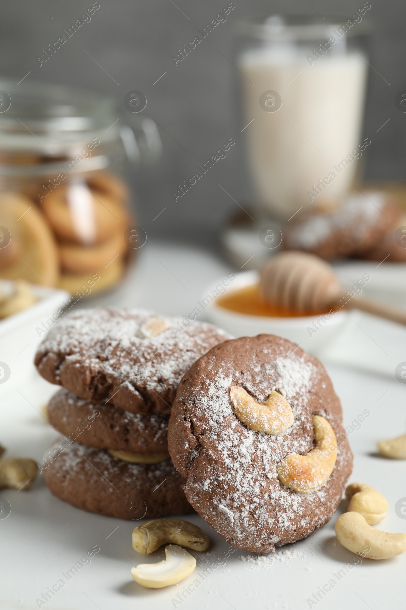 Photo of Tasty chocolate cookies with cashew and powdered sugar on white table, closeup