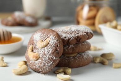 Photo of Tasty chocolate cookies with cashew and powdered sugar on white table, closeup