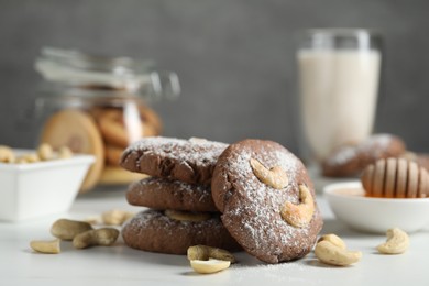 Photo of Tasty chocolate cookies with cashew and powdered sugar on white table, closeup