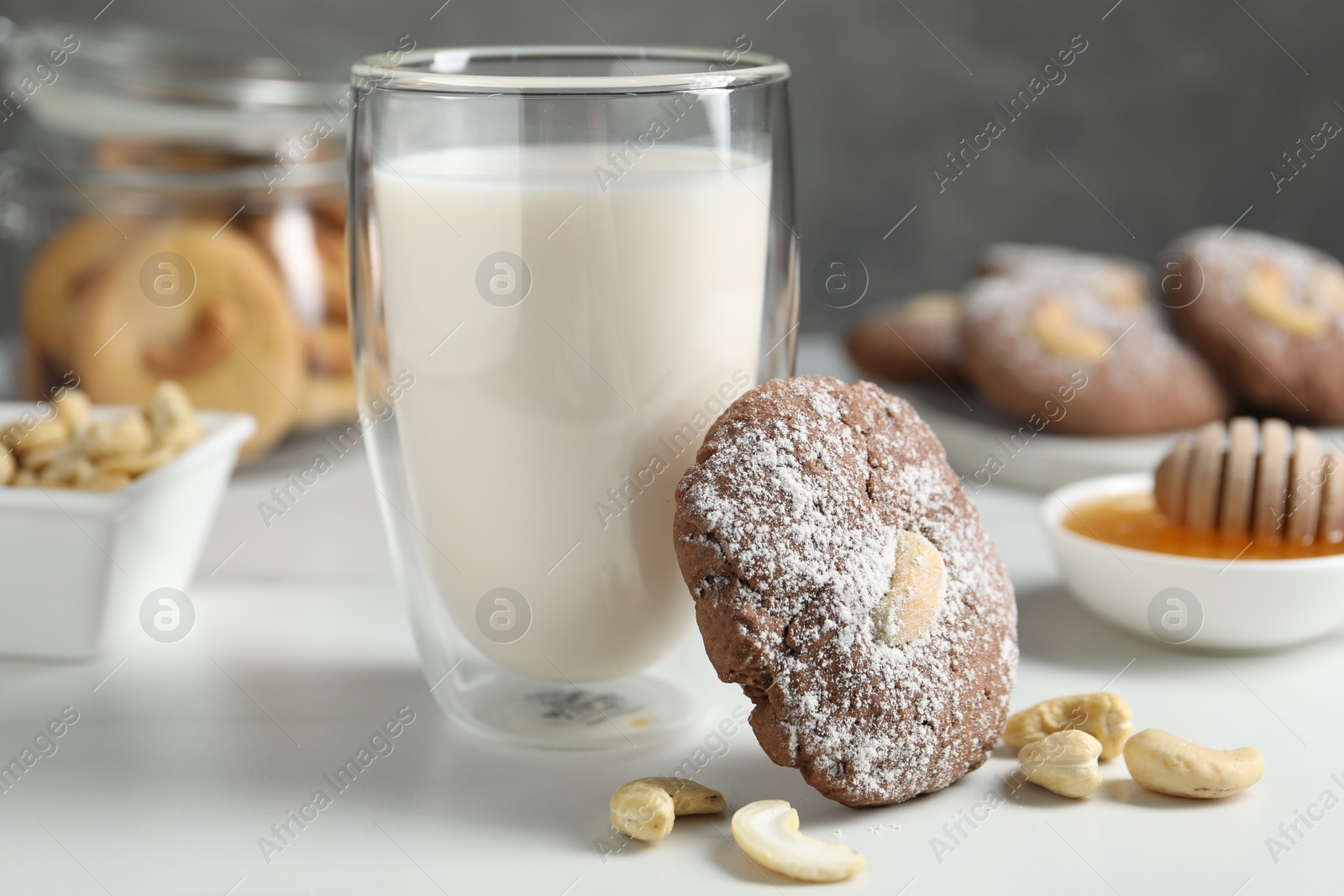 Photo of Tasty chocolate cookie with cashew and glass of milk on white table, closeup