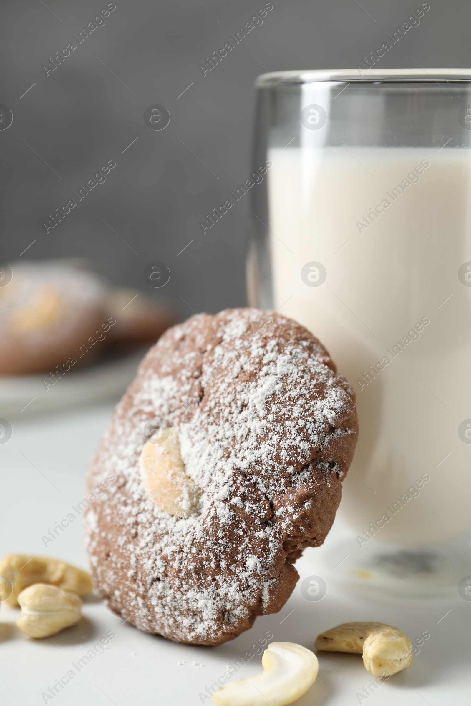 Photo of Tasty chocolate cookie with cashew and glass of milk on white table, closeup