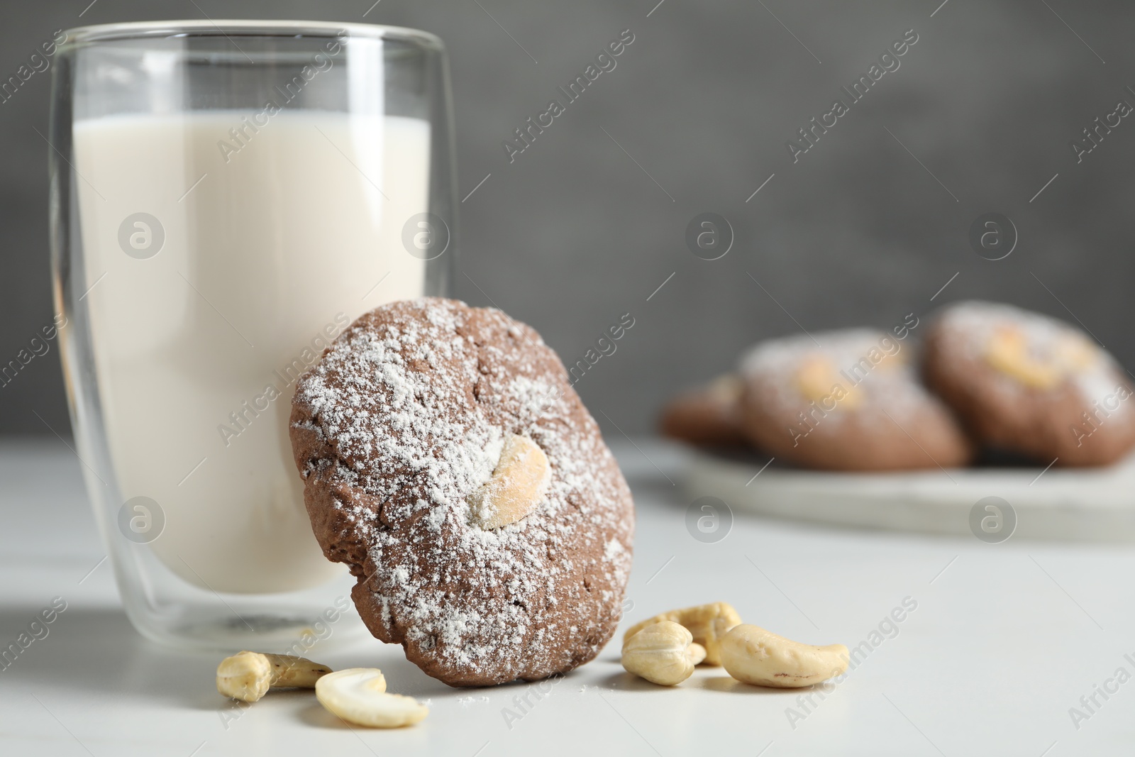 Photo of Tasty chocolate cookie with cashew and glass of milk on white table, closeup. Space for text