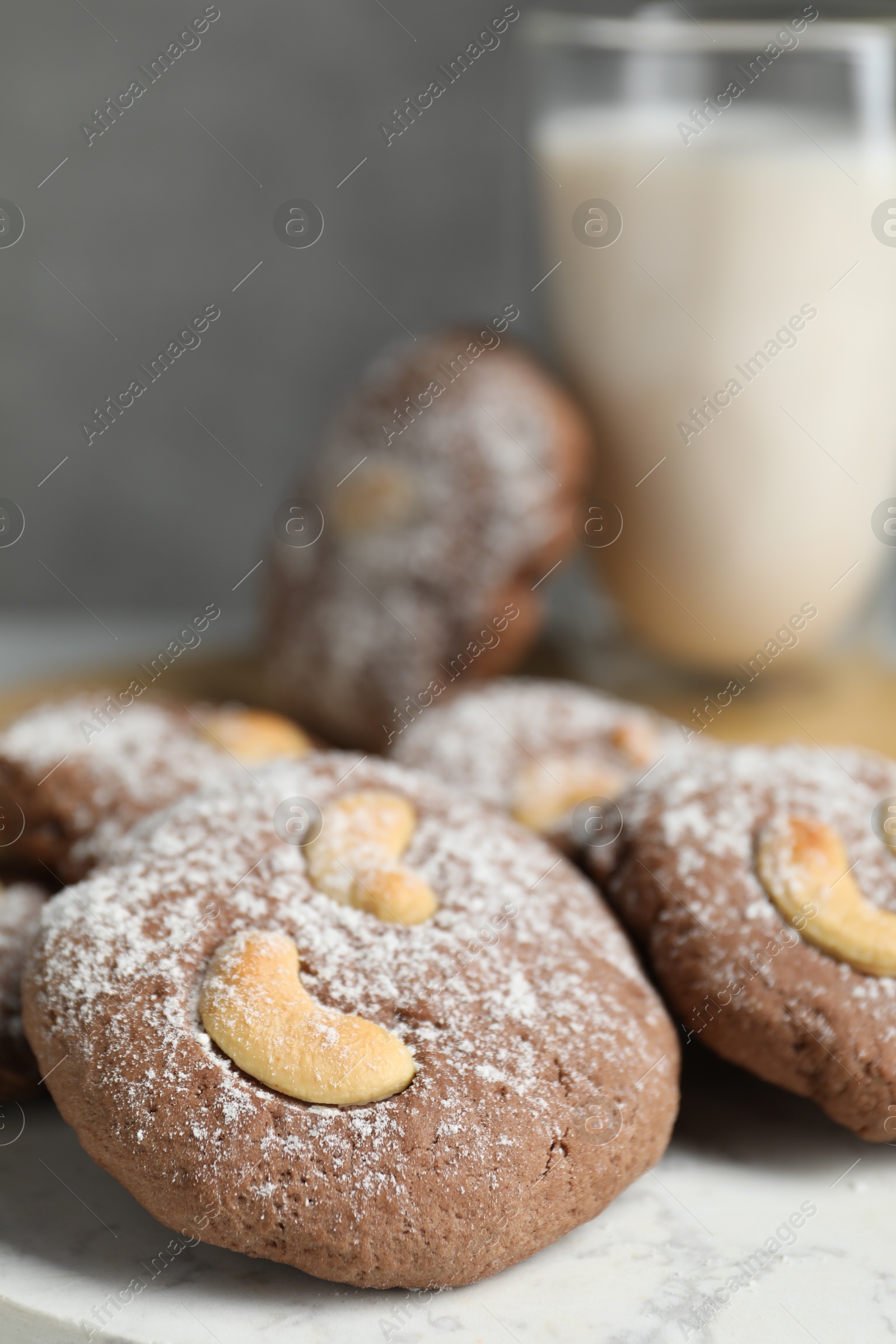 Photo of Tasty chocolate cookies with cashew and powdered sugar on white table, closeup