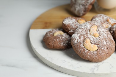 Photo of Tasty chocolate cookies with cashew and powdered sugar on white table, closeup. Space for text