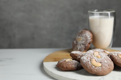 Photo of Tasty chocolate cookies with cashew and powdered sugar on white table, closeup. Space for text