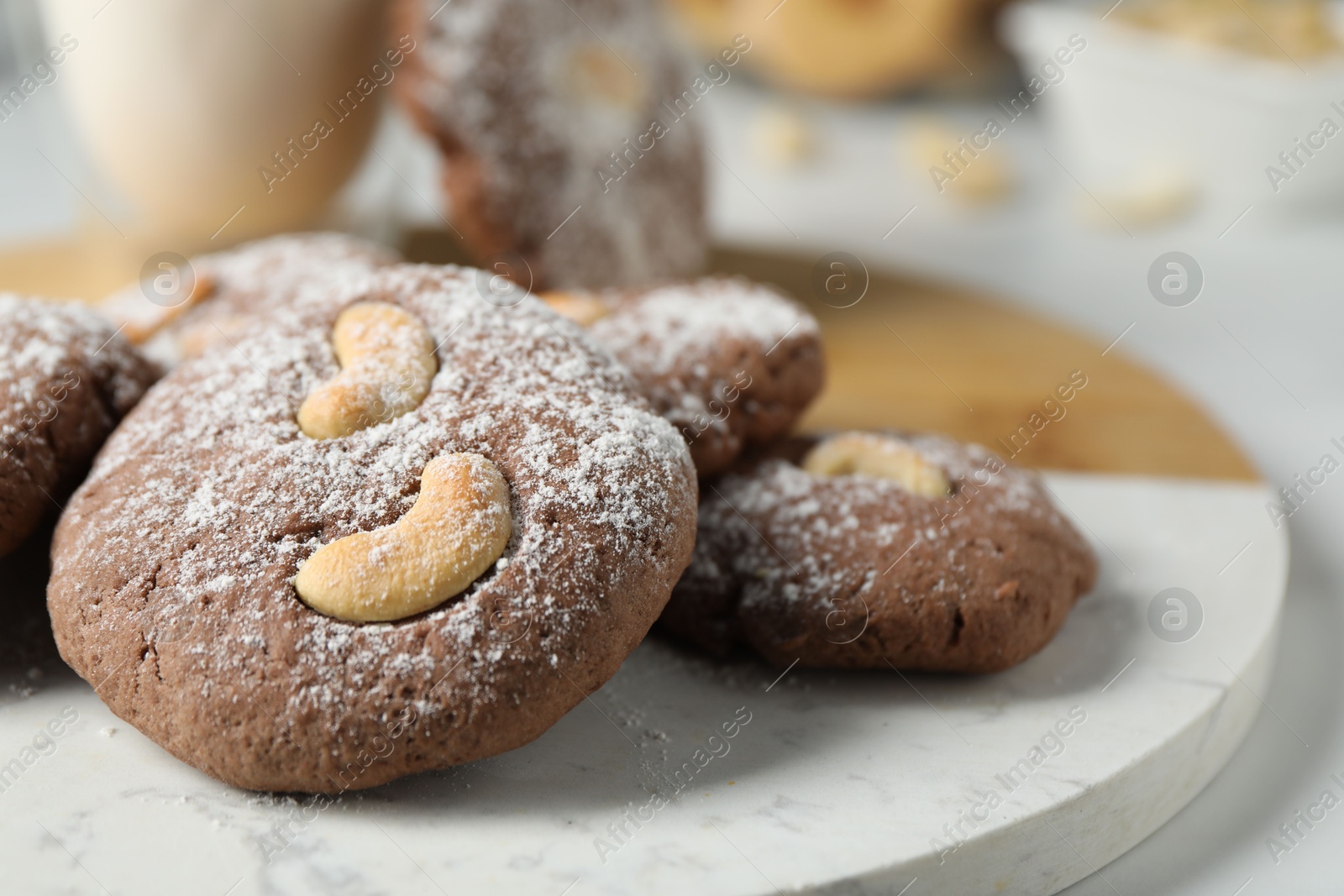 Photo of Tasty chocolate cookies with cashew and powdered sugar on white table, closeup