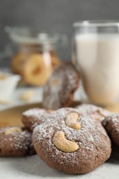 Photo of Tasty chocolate cookies with cashew and powdered sugar on white table, closeup