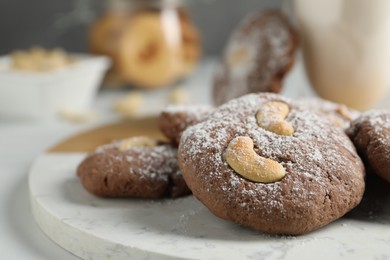 Photo of Tasty chocolate cookies with cashew and powdered sugar on white table, closeup