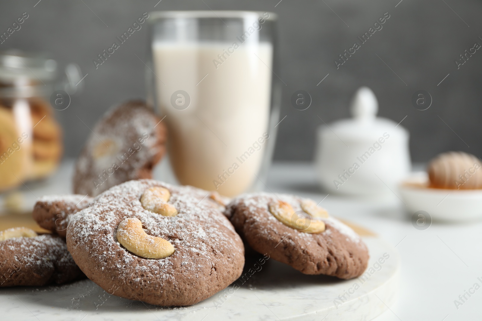 Photo of Tasty chocolate cookies with cashew and powdered sugar on white table, closeup