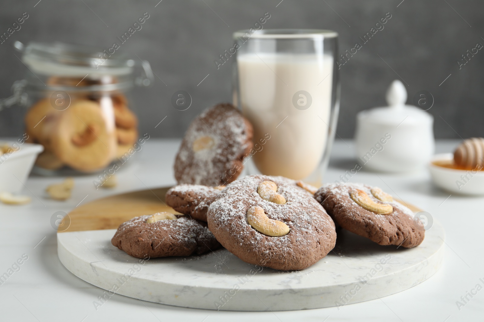 Photo of Tasty chocolate cookies with cashew and powdered sugar on white table, closeup