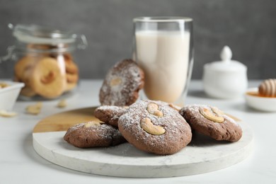 Photo of Tasty chocolate cookies with cashew and powdered sugar on white table, closeup