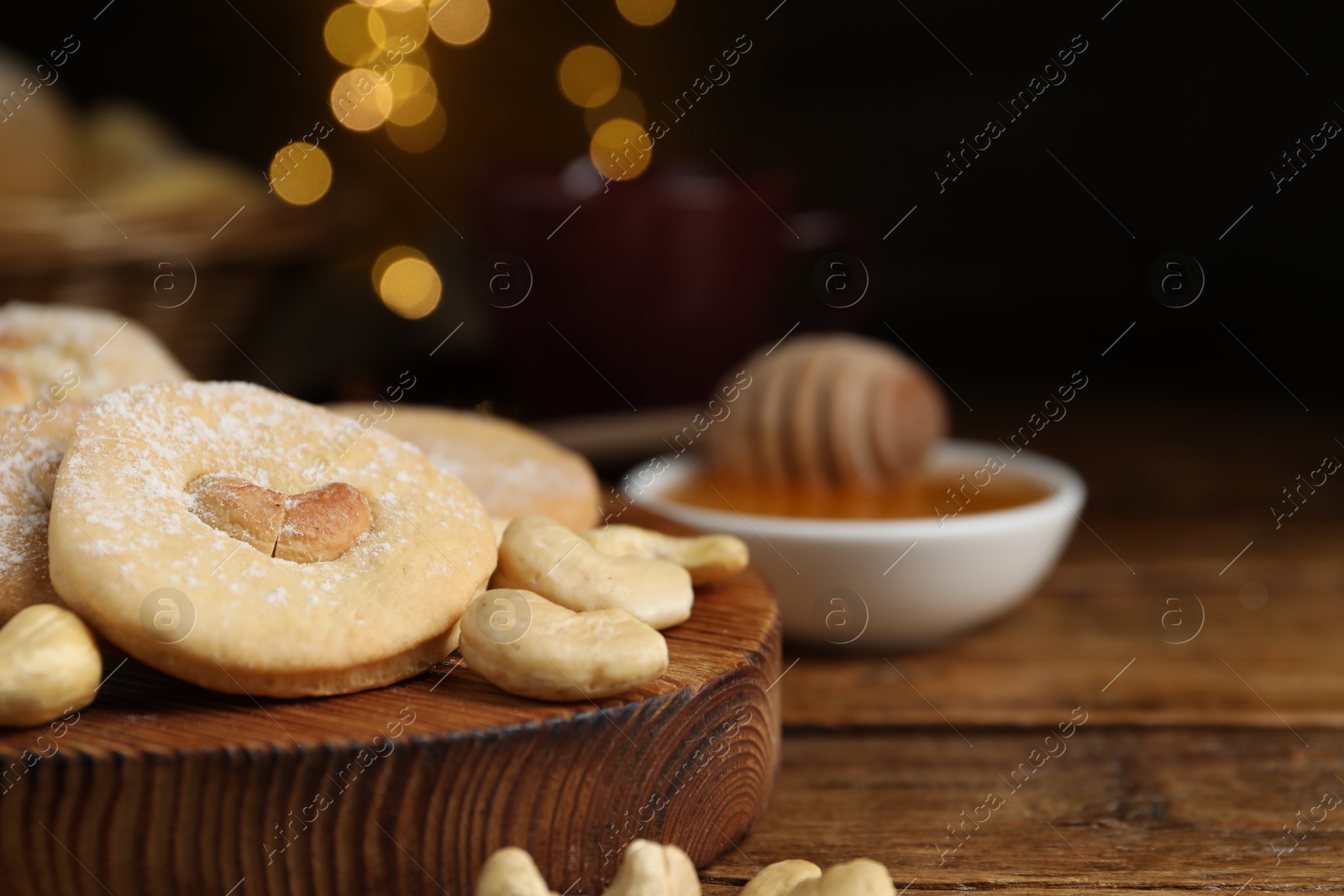 Photo of Tasty cashew cookies with powdered sugar on wooden table, closeup. Space for text