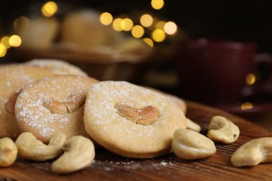 Photo of Tasty cashew cookies with powdered sugar on wooden board, closeup