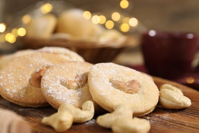 Photo of Tasty cashew cookies with powdered sugar on wooden board, closeup