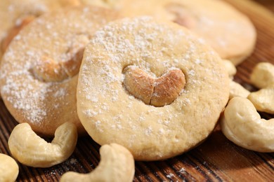 Photo of Tasty cashew cookies with powdered sugar on wooden board, closeup