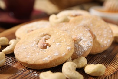 Photo of Tasty cashew cookies with powdered sugar on wooden board, closeup